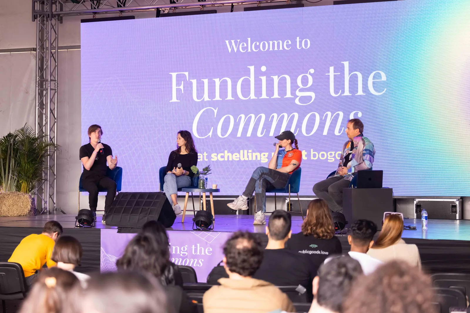 A four-person panel discussion on stage, in front of a "Funding the Commons" banner.