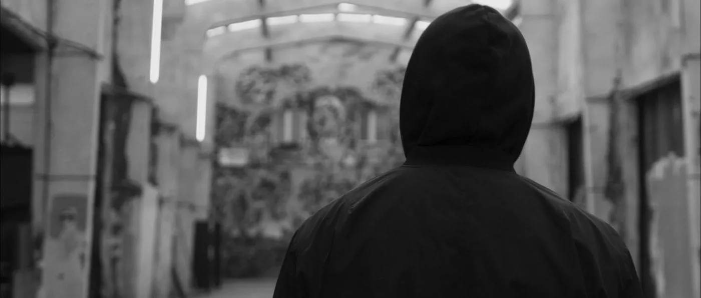 A hooded figure before a fresco-covered wall.